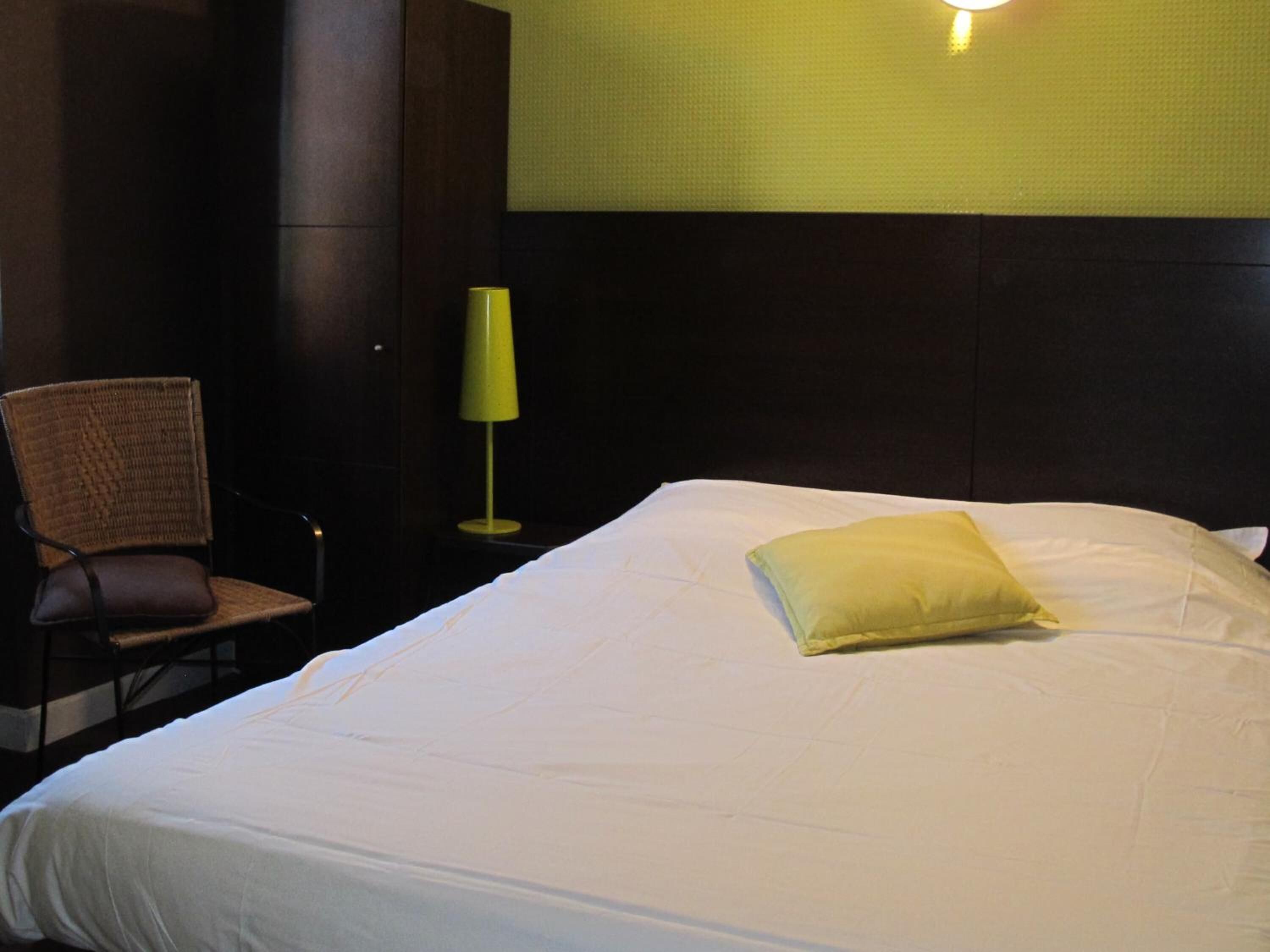 Habitación de hotel con una cama grande, una silla y una mesita de noche con lámpara.