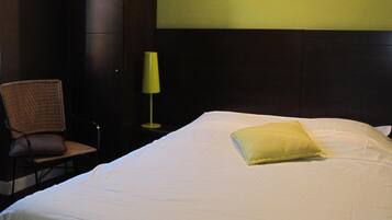 Habitación de hotel con una cama grande, una silla y una mesita de noche con lámpara.