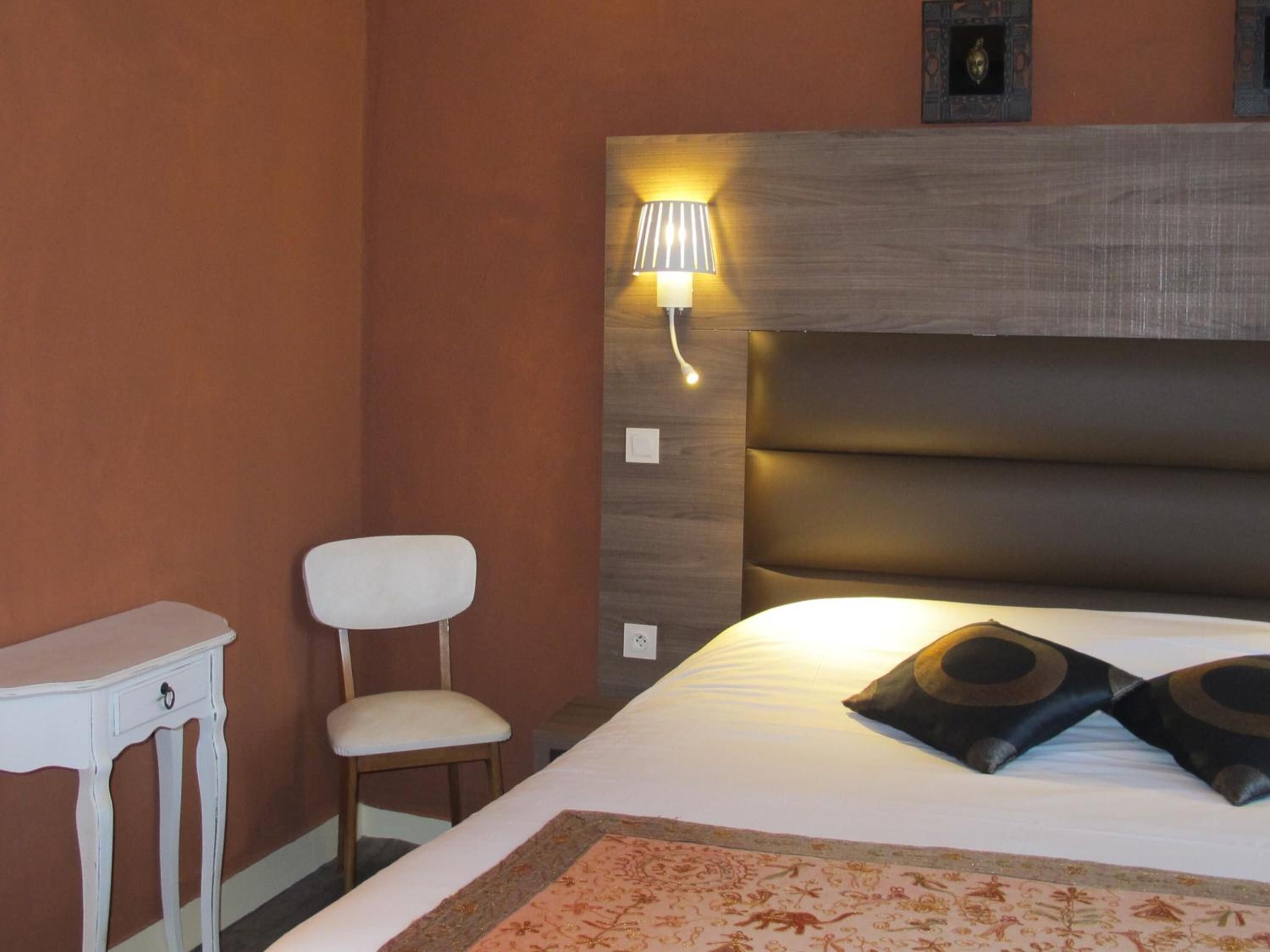 Ein Hotelzimmer mit Bett, Stuhl, kleinem Tisch und Wandlampe.