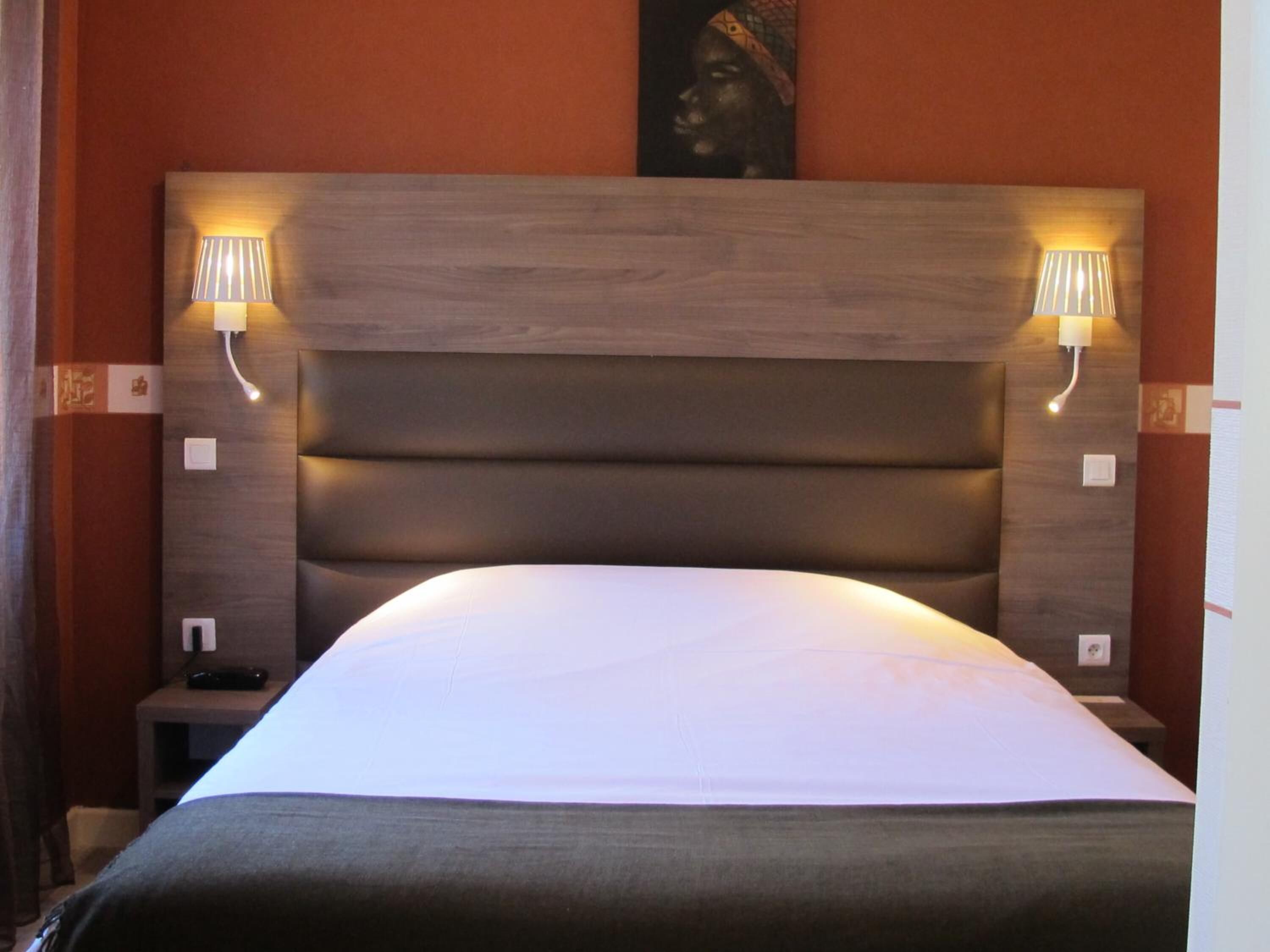 Habitación de hotel con una cama grande, cabecero de madera, dos lámparas de noche y una mesita de noche con un teléfono.