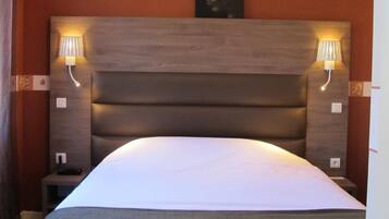 Habitación de hotel con una cama grande, cabecero de madera, dos lámparas de noche y una mesita de noche con un teléfono.