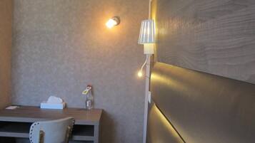Ein Hotelzimmer mit einem hölzernen Kopfteil, einem Nachttisch mit Lampe, einem Sessel und einem kleinen Schreibtisch mit Taschentuchbox und Flasche.