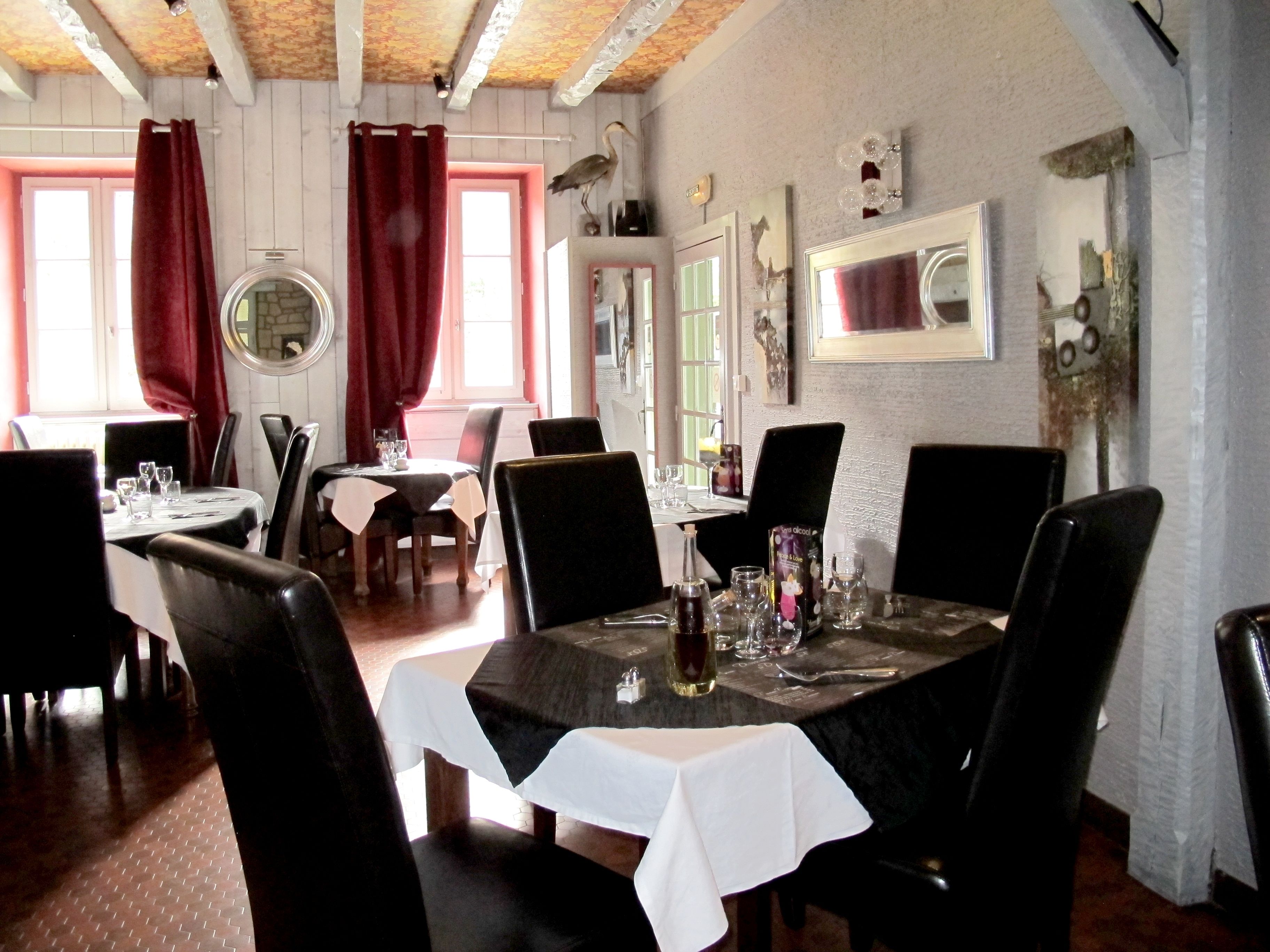 Un comedor con mesas dispuestas para cuatro, cortinas rojas y un pájaro posado en la pared.