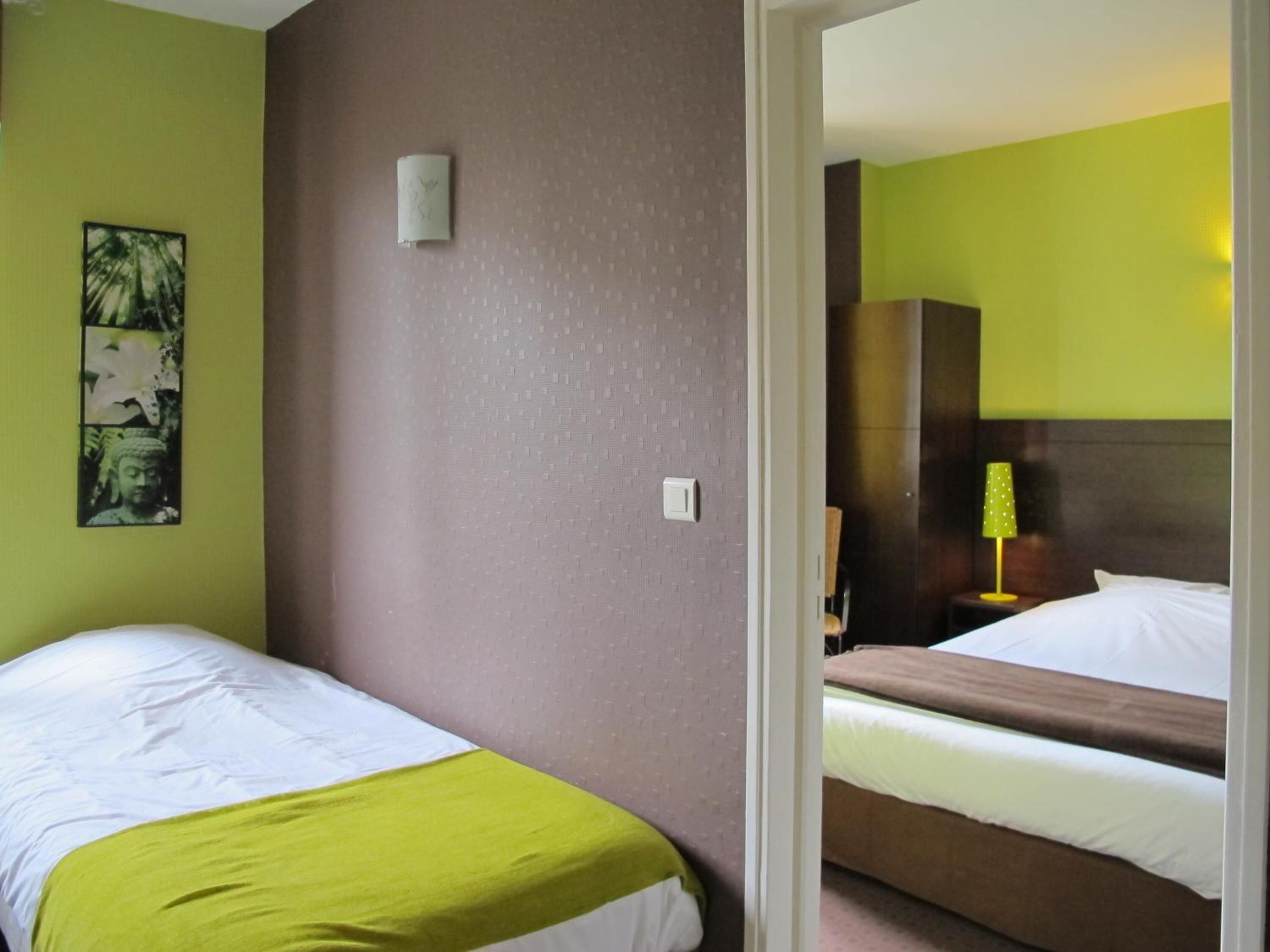 A hotel room with two beds, a green wall, a Buddha statue, and a lamp.