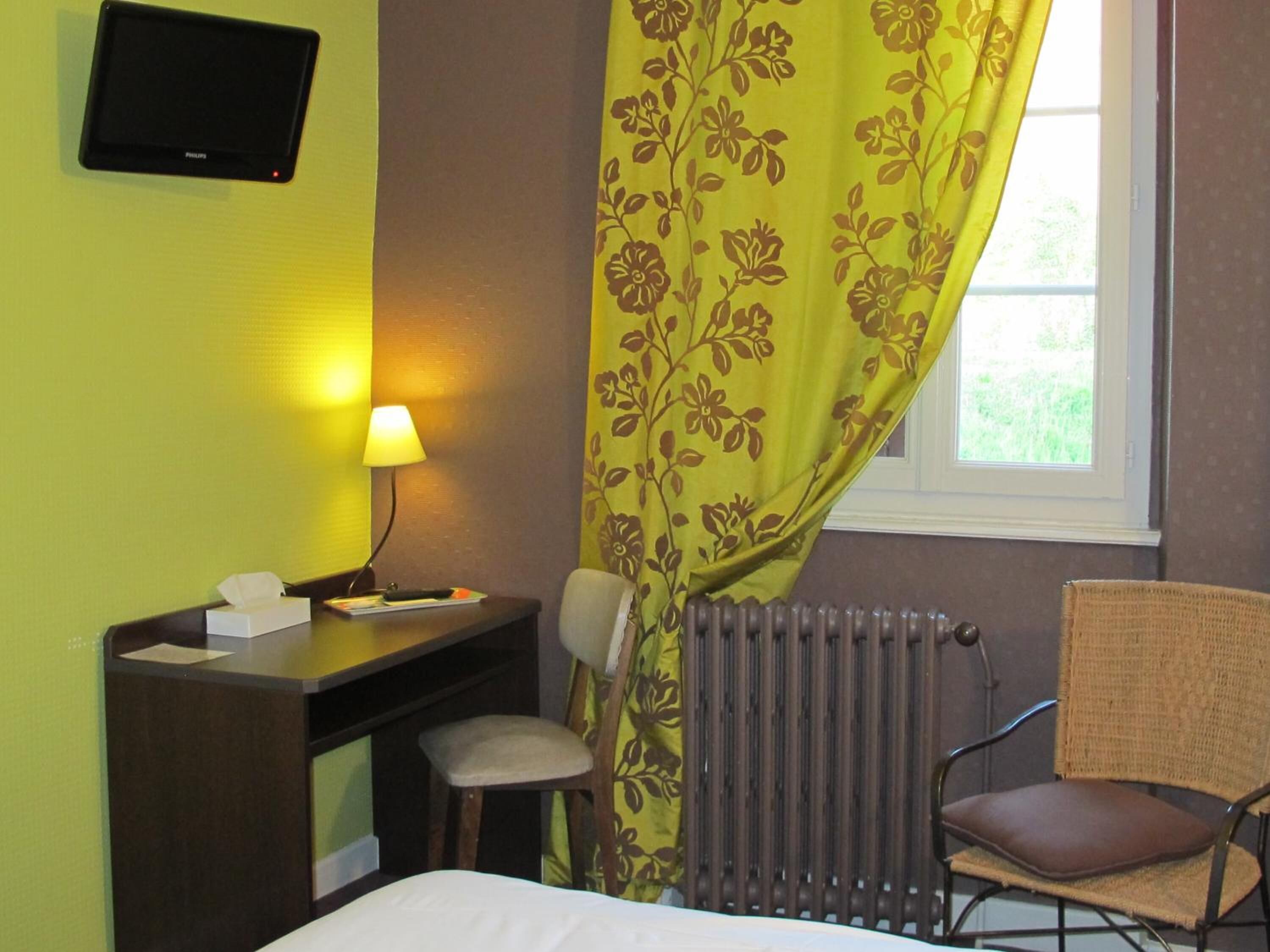 Een hotelkamer met een bed, een bureau met een stoel, een televisie, een raam met uitzicht en een radiator.
