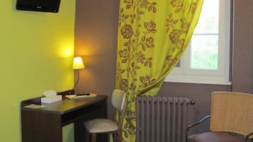 Een hotelkamer met een bed, een bureau met een stoel, een televisie, een raam met uitzicht en een radiator.