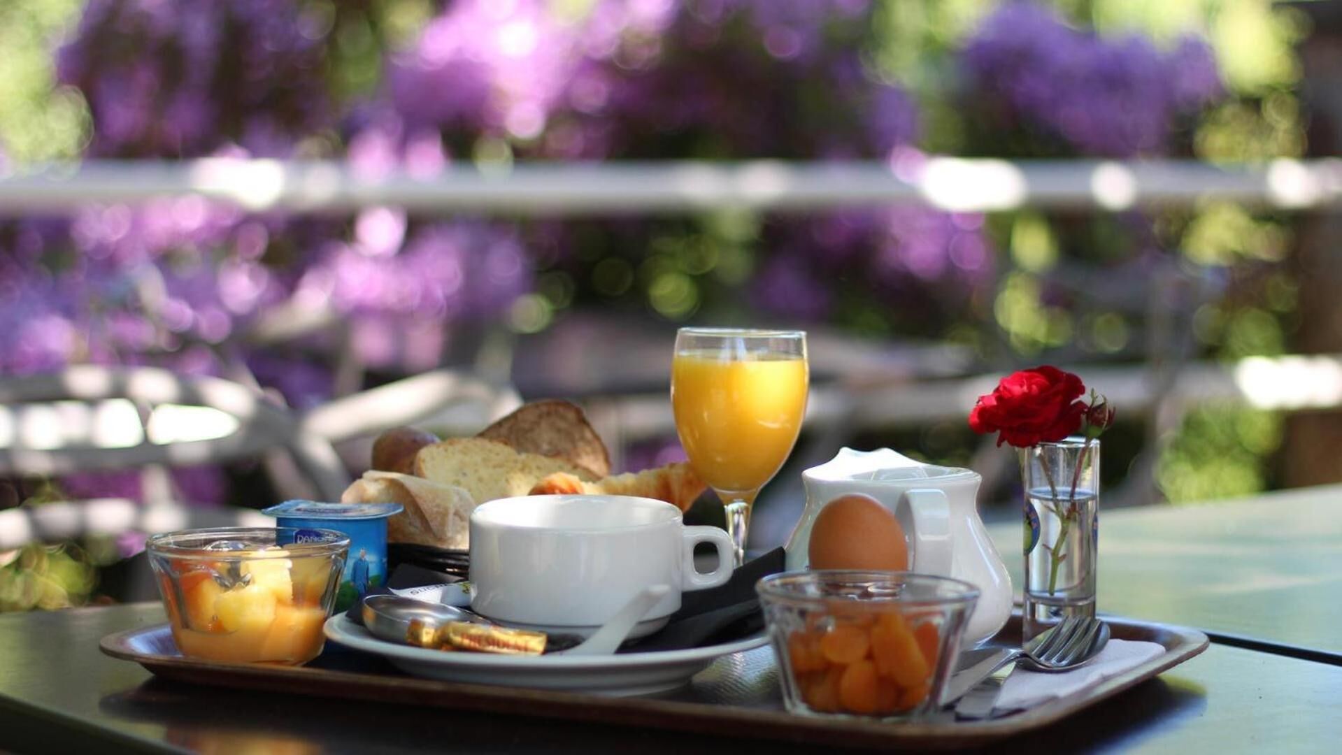 A breakfast tray with toast, eggs, orange juice, and a rose in a vase.