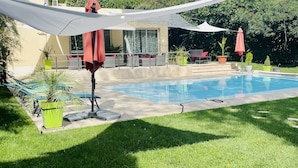 A swimming pool with lounge chairs and umbrellas, surrounded by greenery and a building. - The Originals City, Hôtel Costières, Nîmes (Nîmes)