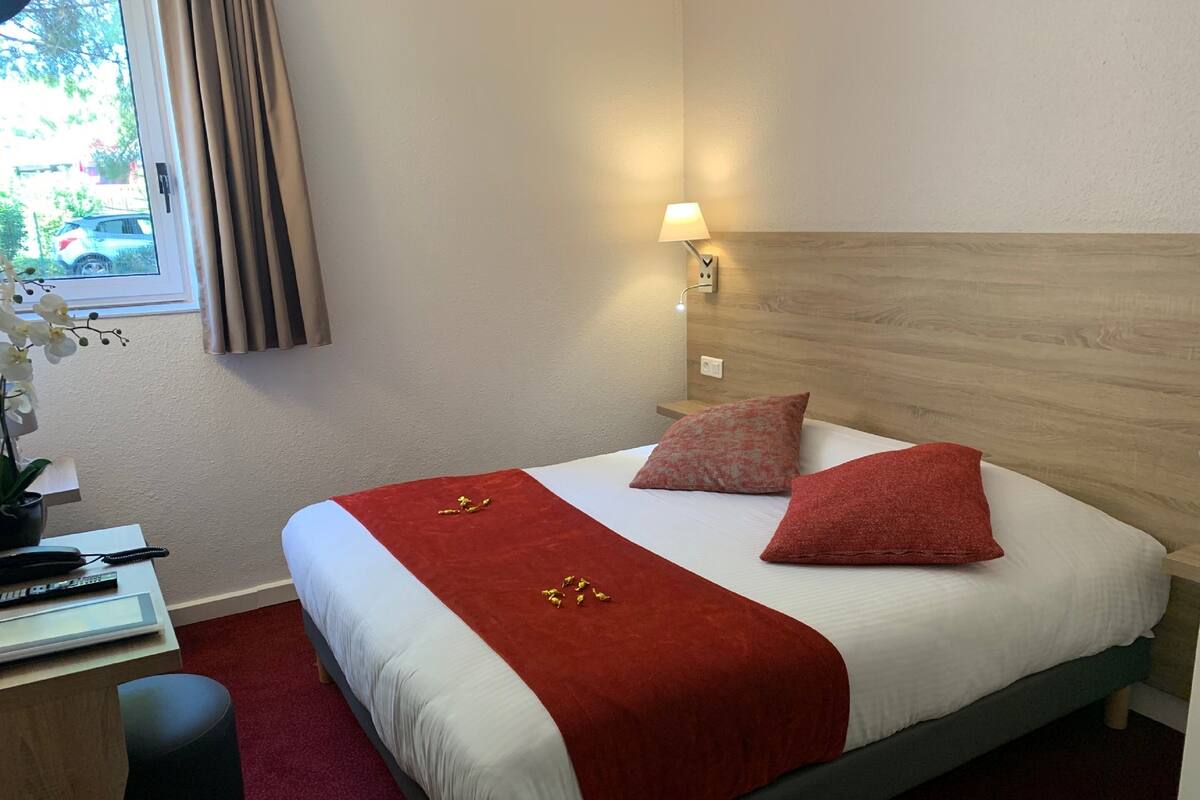 Une chambre d’hôtel avec un lit, un bureau, une lampe et une fenêtre avec des rideaux.