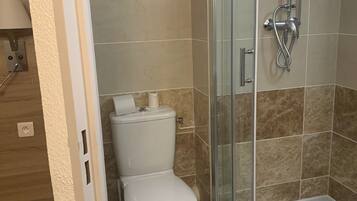 A bathroom with a toilet, a glass-enclosed shower, and a towel hanging on the shower door.
