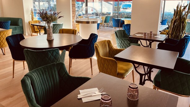 A modern dining area with round tables and vibrant chairs, large windows with a view of parked cars, and a central pillar. - The Originals City, Hôtel Costières, Nîmes (Nîmes)