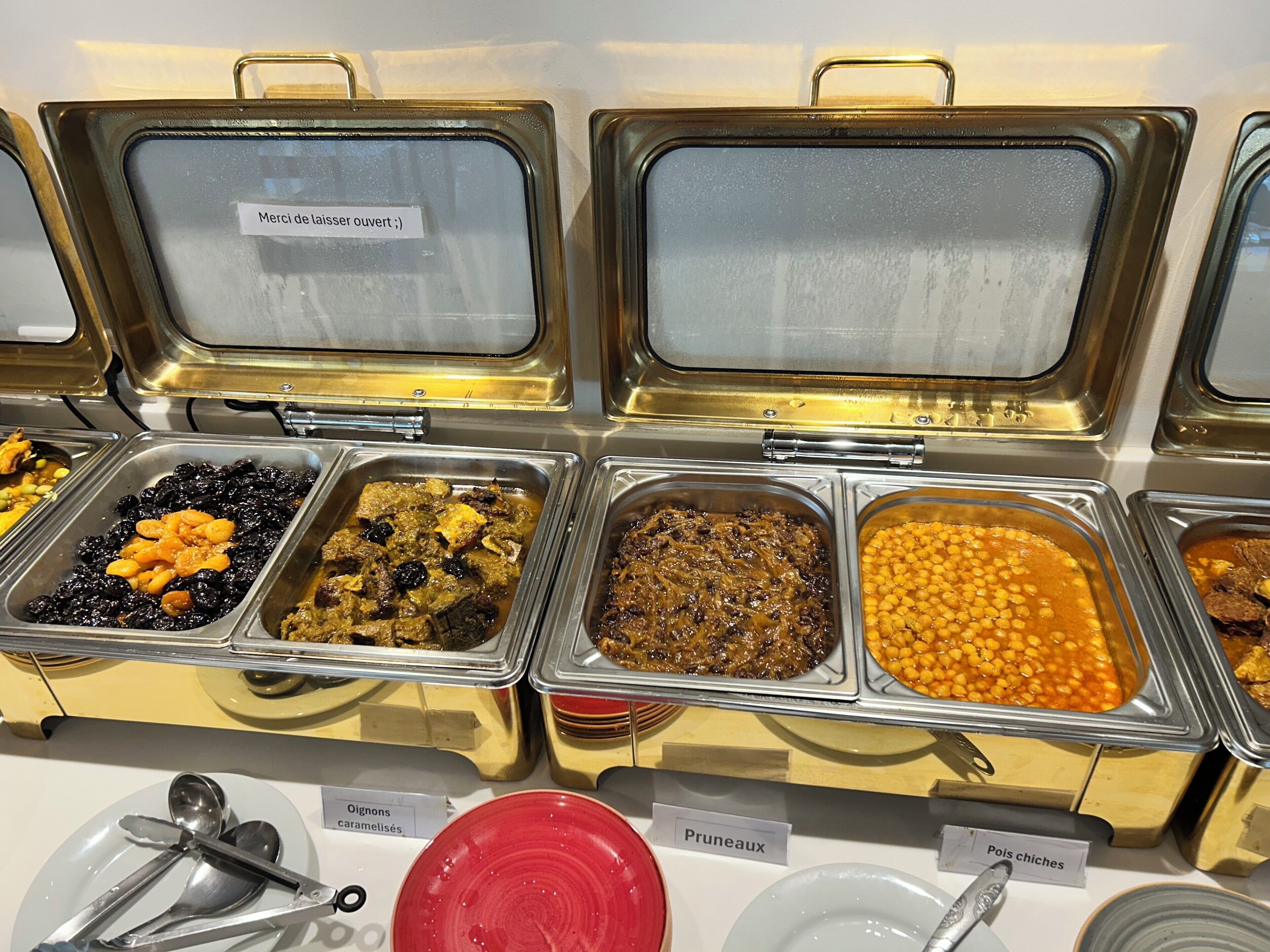 Un bufé con diversas opciones de comida, entre ellas frijoles, platos de carne y un plato rojo.