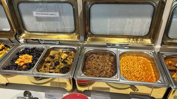 Un bufé con diversas opciones de comida, entre ellas frijoles, platos de carne y un plato rojo.