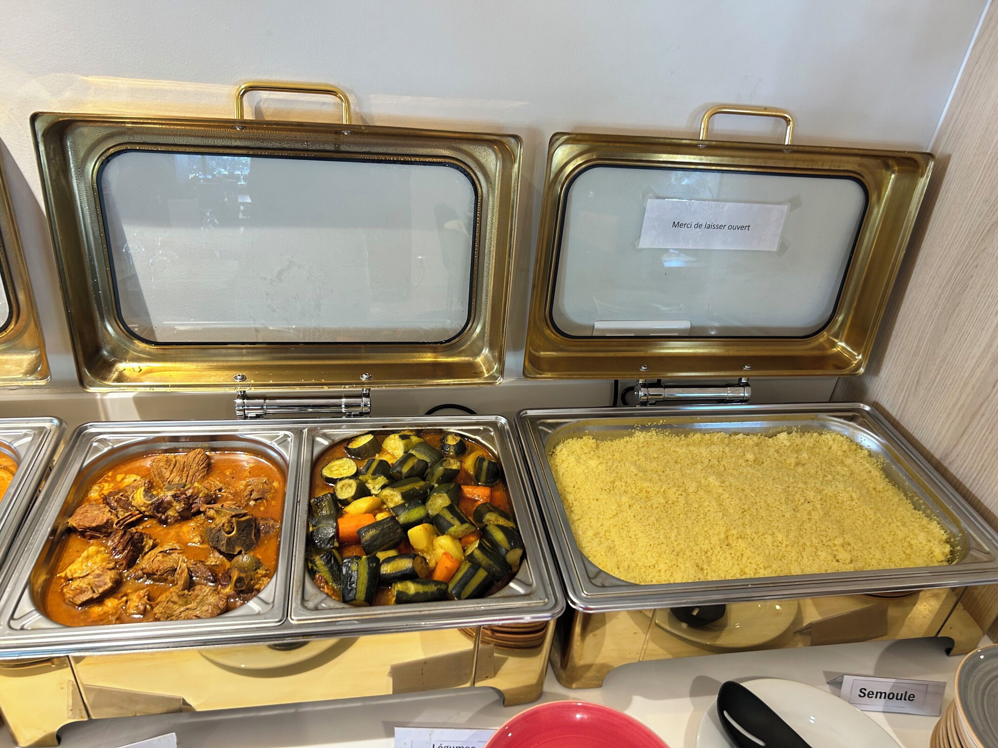 Un buffet con diversi piatti, tra cui un piatto di carne, uno di verdure e un piatto di couscous.