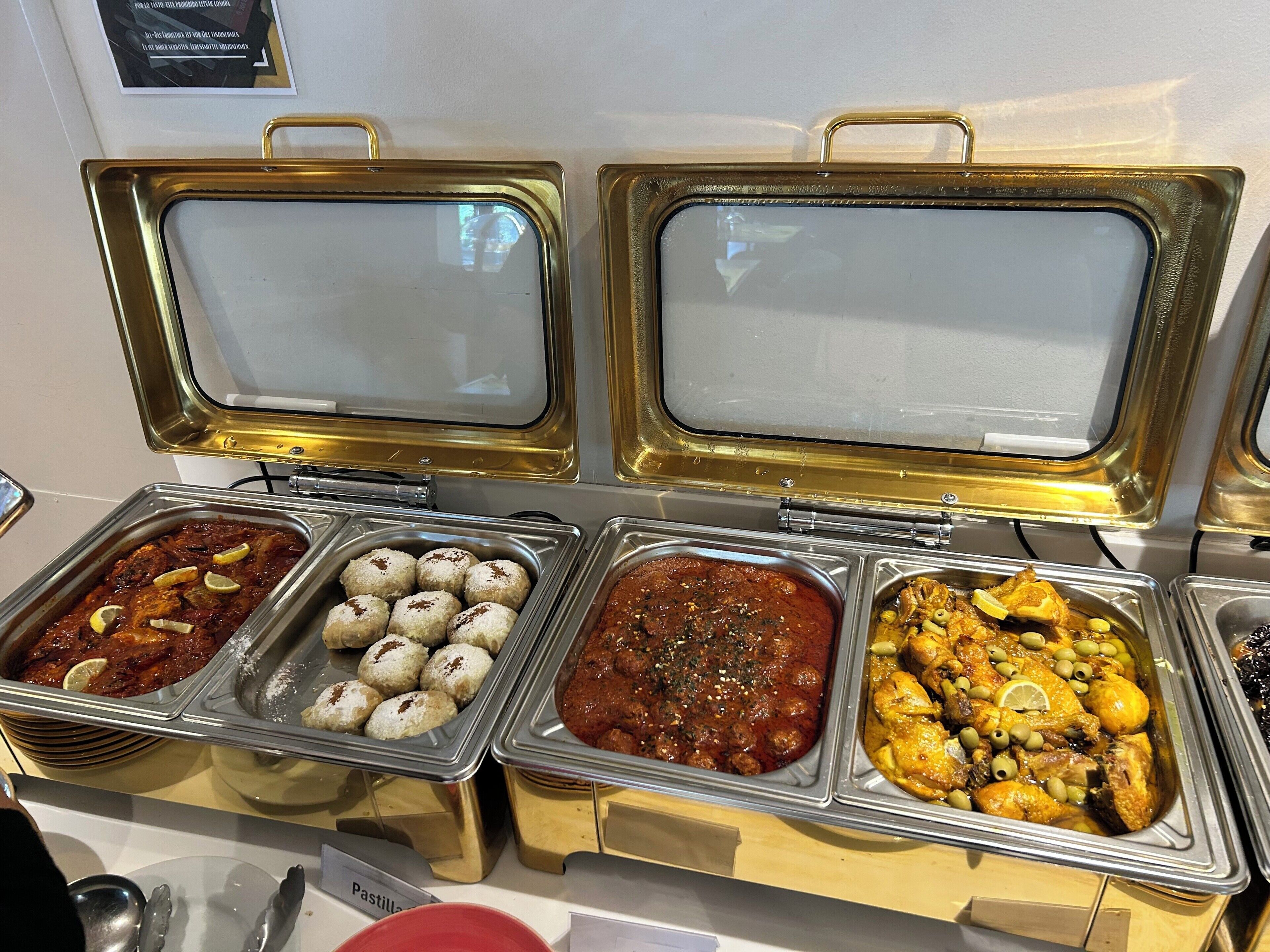 En buffet med forskellige retter, herunder en rød sauce, citronskiver og en kyllingeret med oliven.