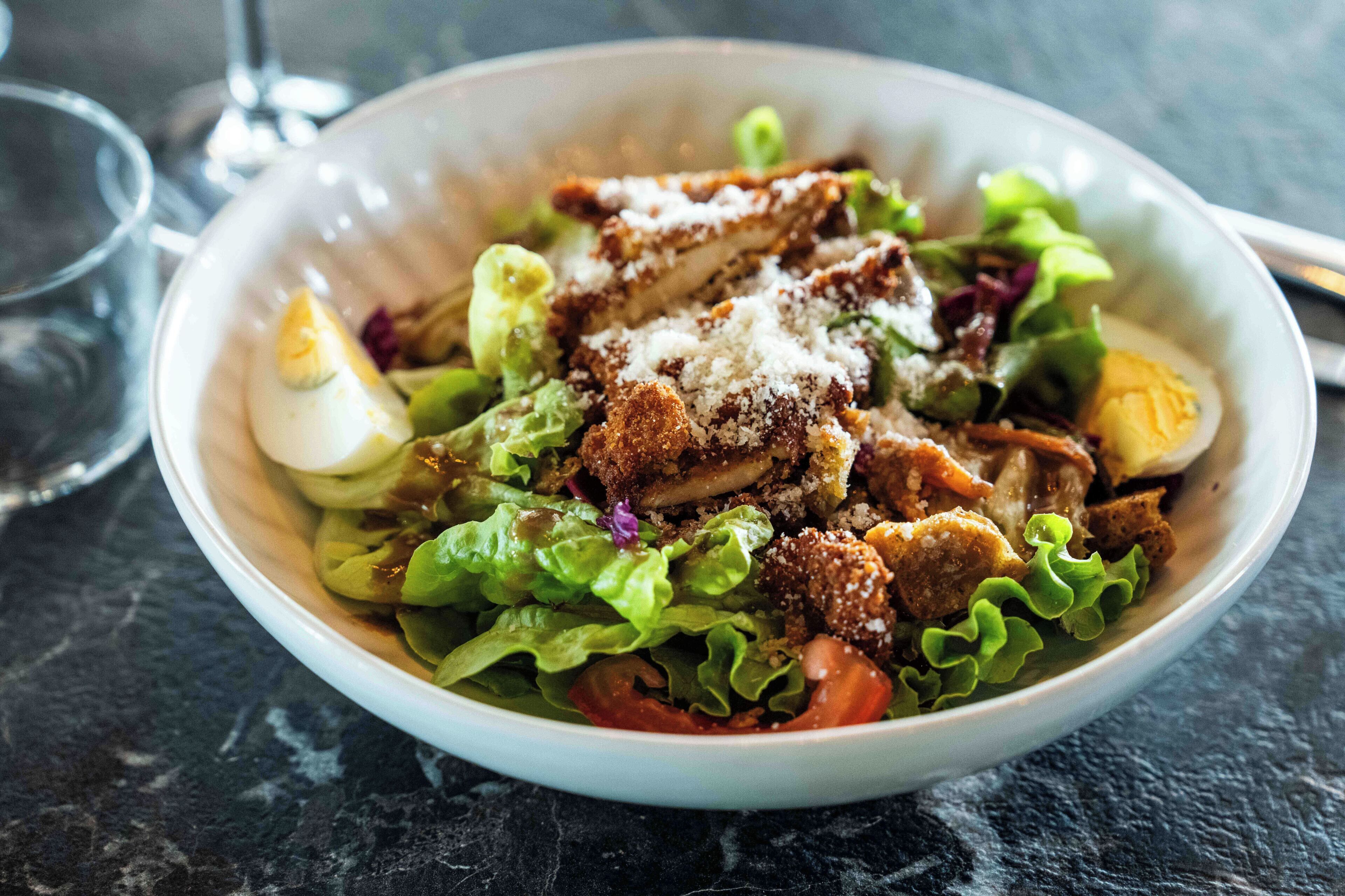 A bowl of salad with lettuce, tomatoes, and a hard-boiled egg.