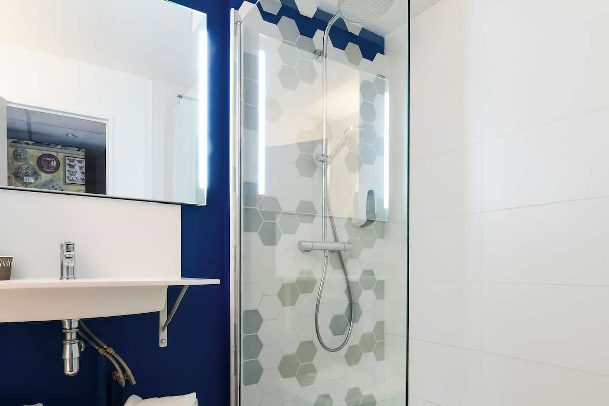Un baño moderno con ducha de vidrio, un lavabo blanco con un espejo encima y piso de madera.