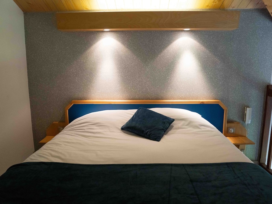 A bed with a blue headboard, a white pillow, and a dark blue blanket. There are two bedside tables with lamps.