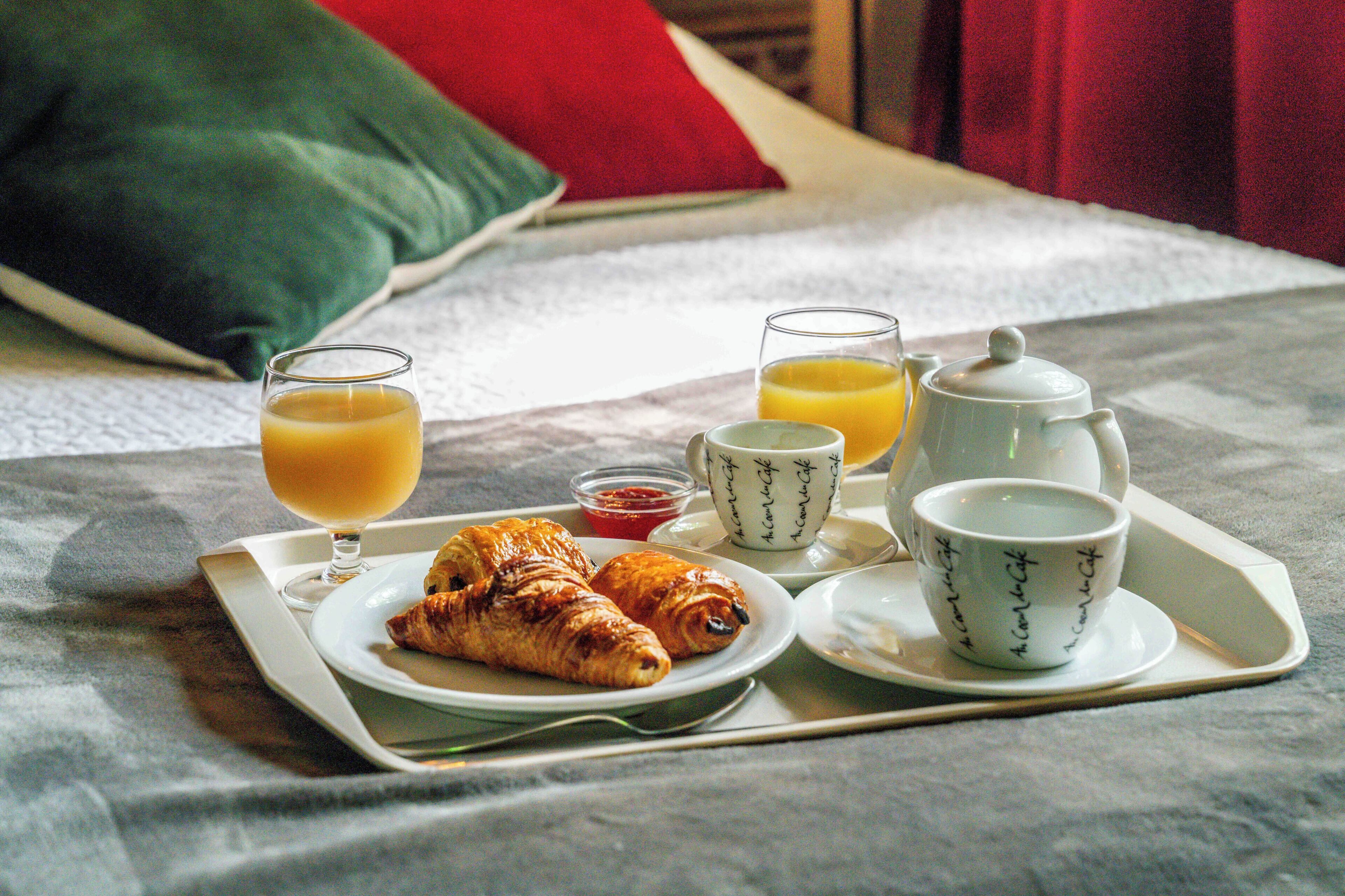 Bandeja de desayuno en una cama con cruasanes, zumo de naranja y tazas de café.