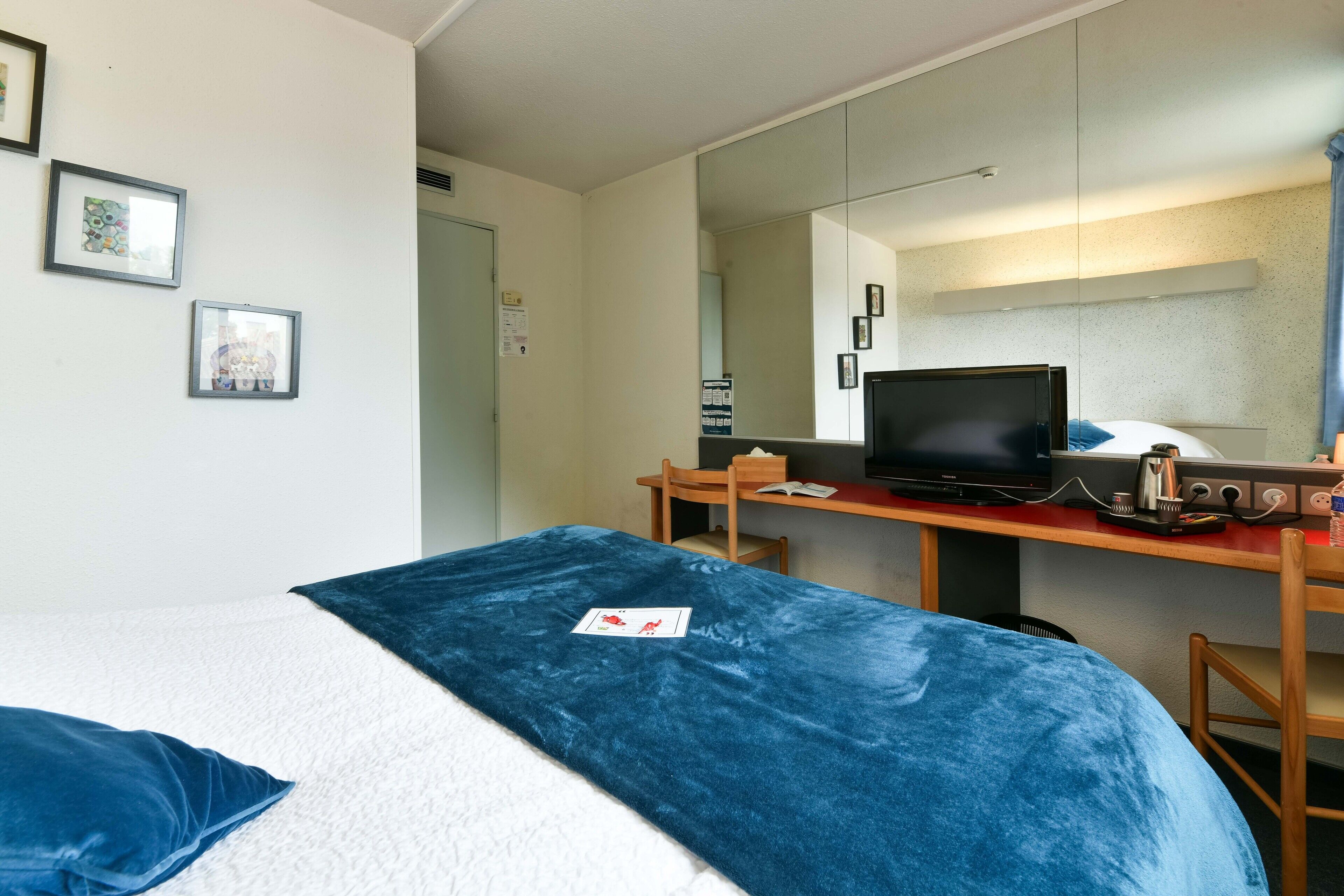 Una habitación de hotel con una cama, un escritorio con computadora, televisor y espejo.
