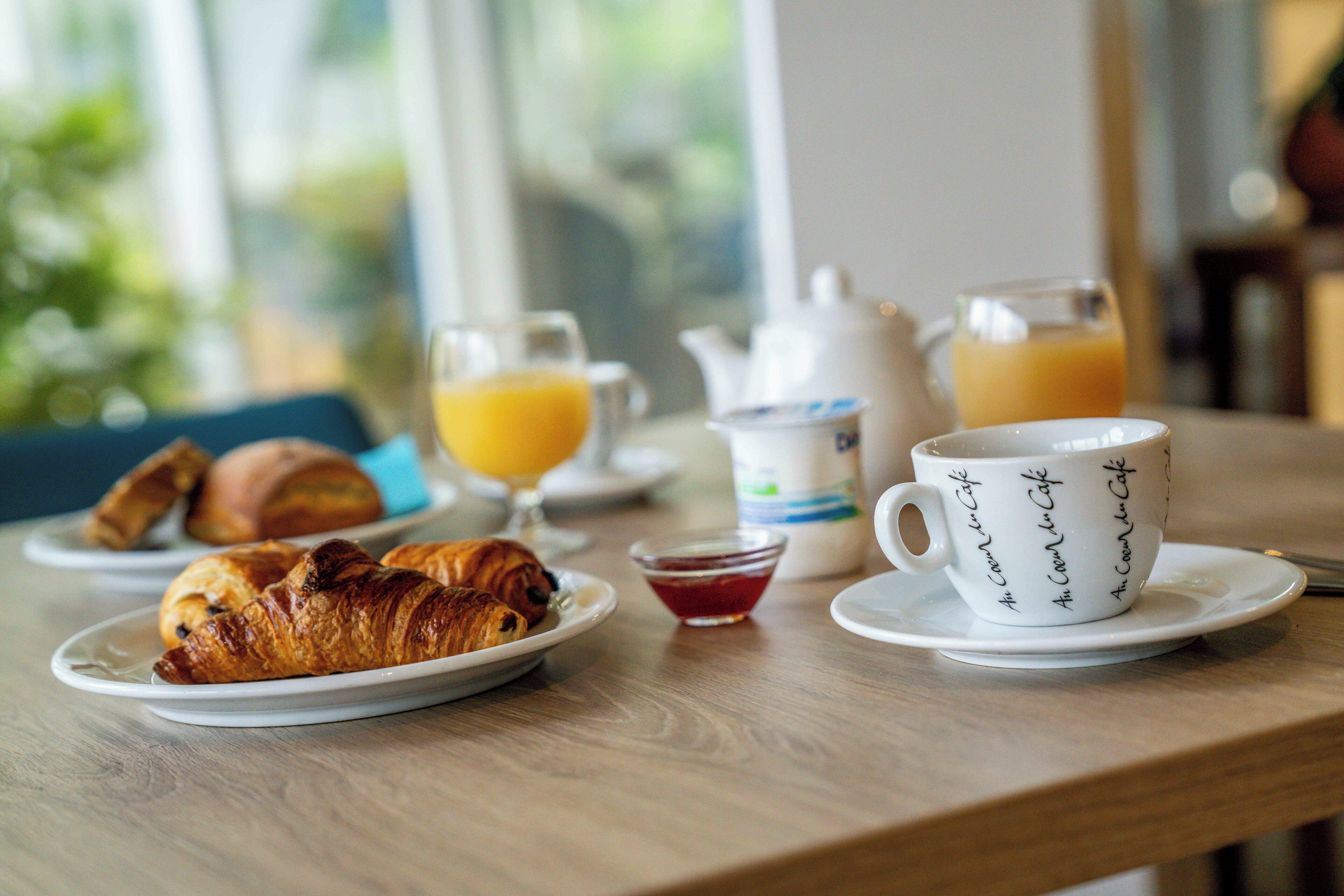 A breakfast table with croissants, a cup of coffee, a glass of orange juice, and a pitcher of milk.