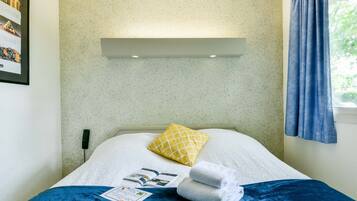A neatly made bed with a white and blue bedspread, a yellow patterned pillow, and a folded towel.