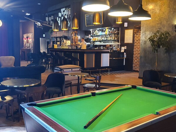 Uma mesa de bilhar em área de bar, com um bartender atrás do balcão.