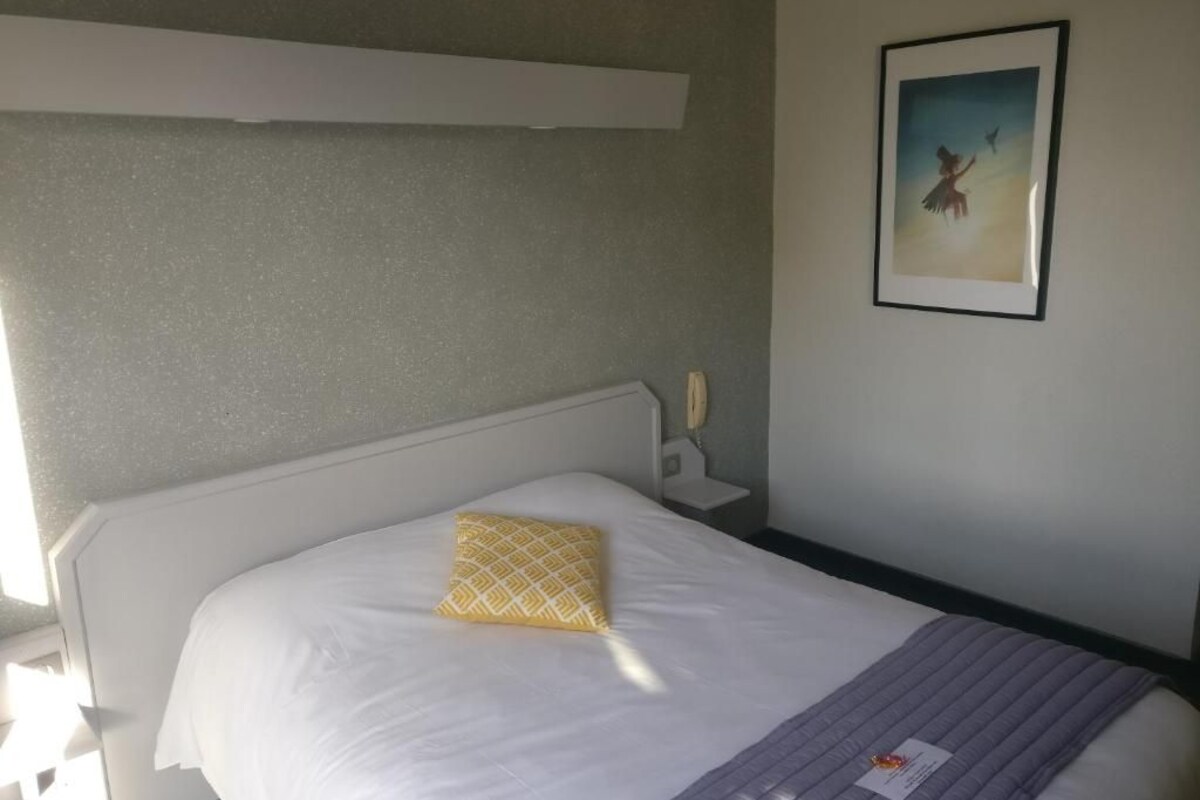 Habitación de hotel con una cama, una mesita de noche, un cuadro enmarcado en la pared y una ventana.