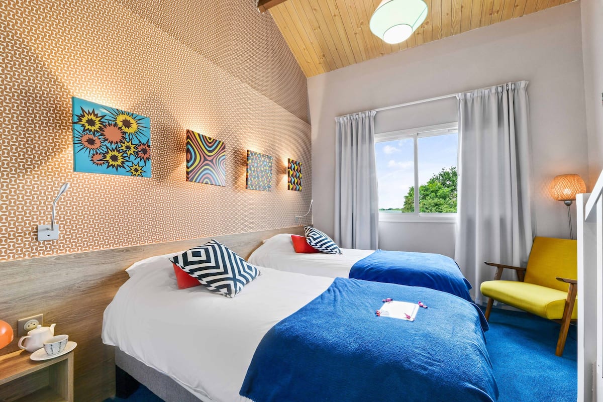 Habitación de hotel con dos camas, techo de madera, ventana con cortinas y una obra de arte en la pared.