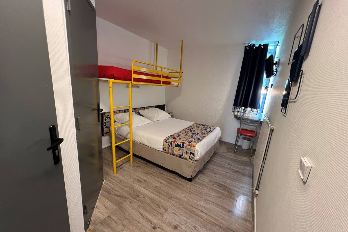 A small, compact room with a bunk bed, a desk with a chair, and a small stool.