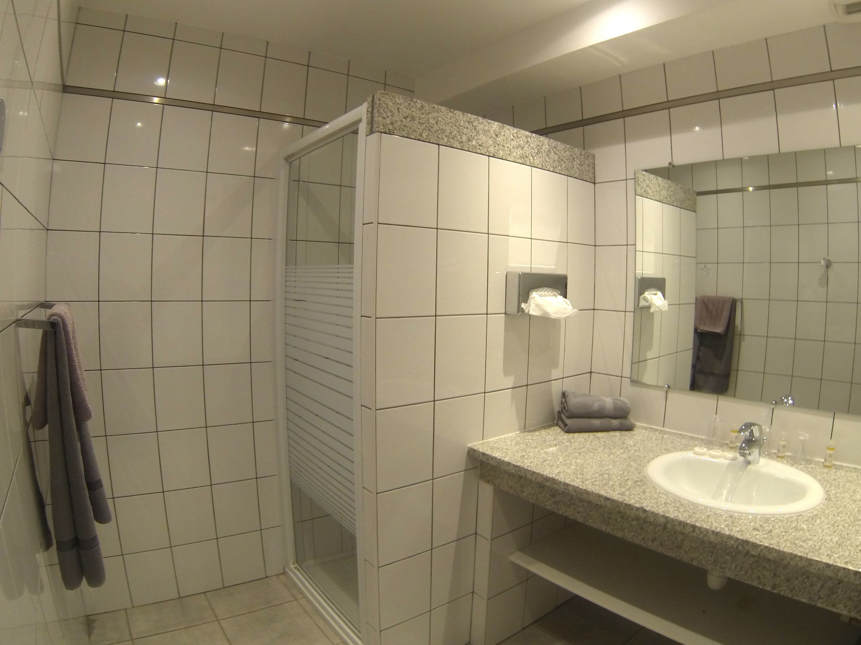 Un baño moderno con azulejos blancos, lavamanos de granito, espejo y cabina de ducha con mampara de vidrio.