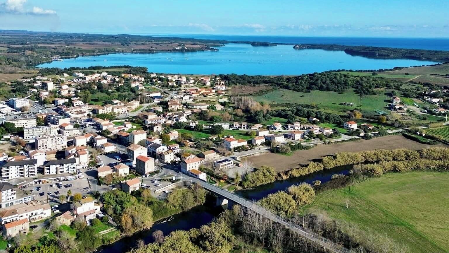 Vista aérea de un pueblo costero con un río que lo atraviesa, un puente cruzando el río y edificios a lo largo de la ribera.