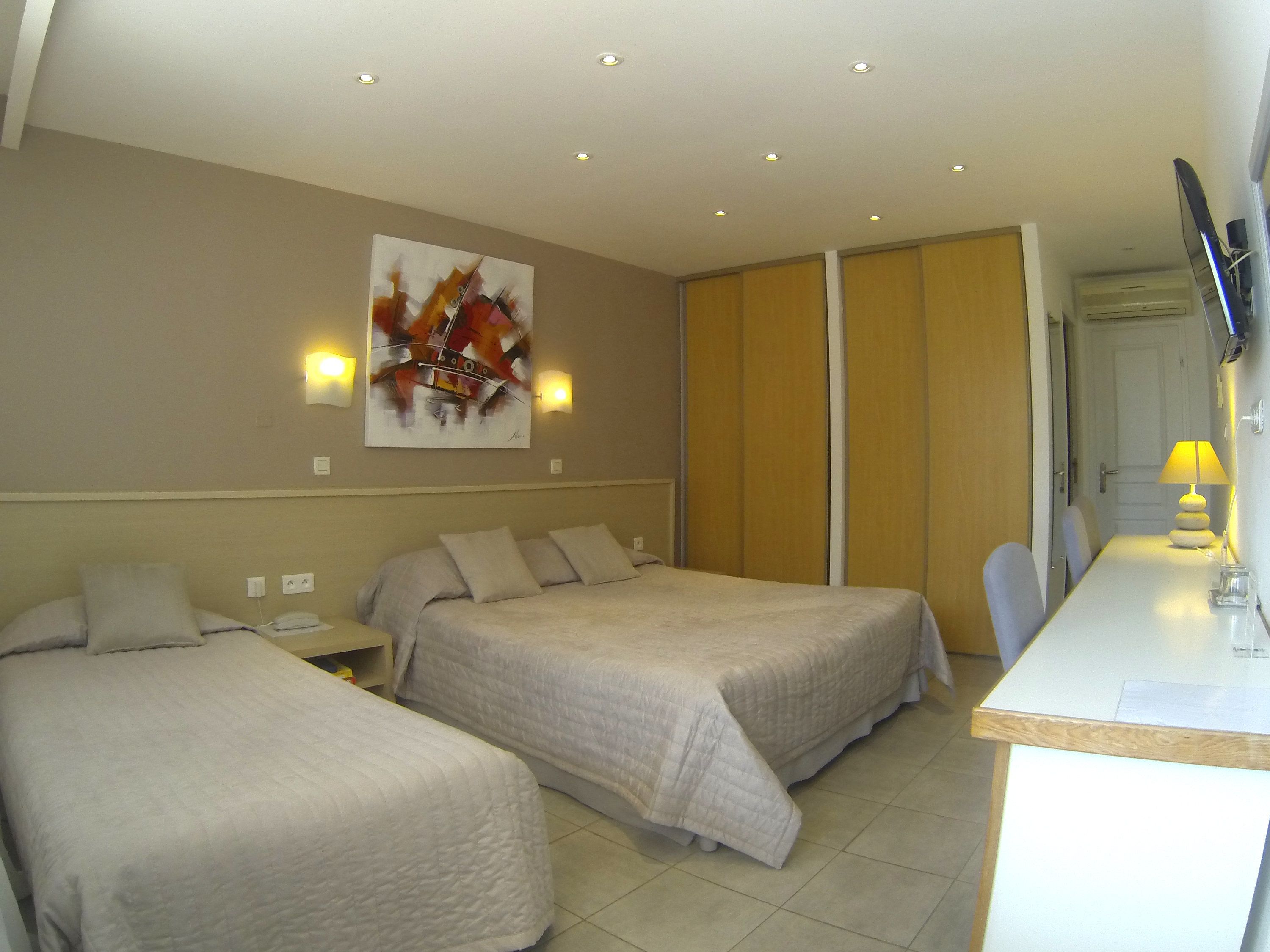 A hotel room with two beds, a desk with a lamp, a TV, and a painting on the wall.