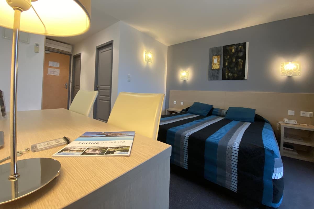 A hotel room with a bed, bedside tables, a desk with a lamp, and a chair.