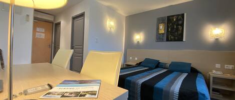 A hotel room with a bed, bedside tables, a desk with a lamp, and a chair.