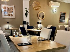 Un comedor con una mesa de madera, sillas blancas, una obra de arte enmarcada, un espejo y un tablero de menú.