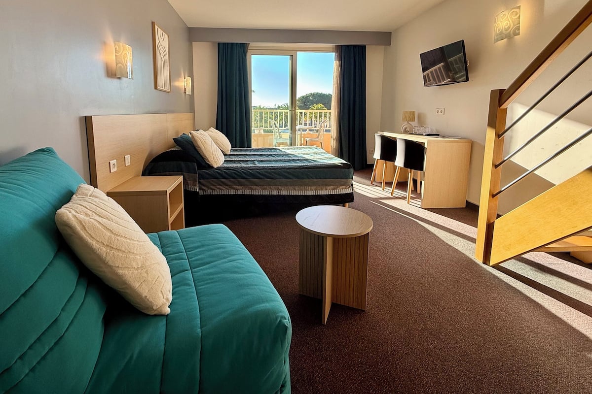 A hotel room with a bed, a sofa, a small table, a desk, and a TV.