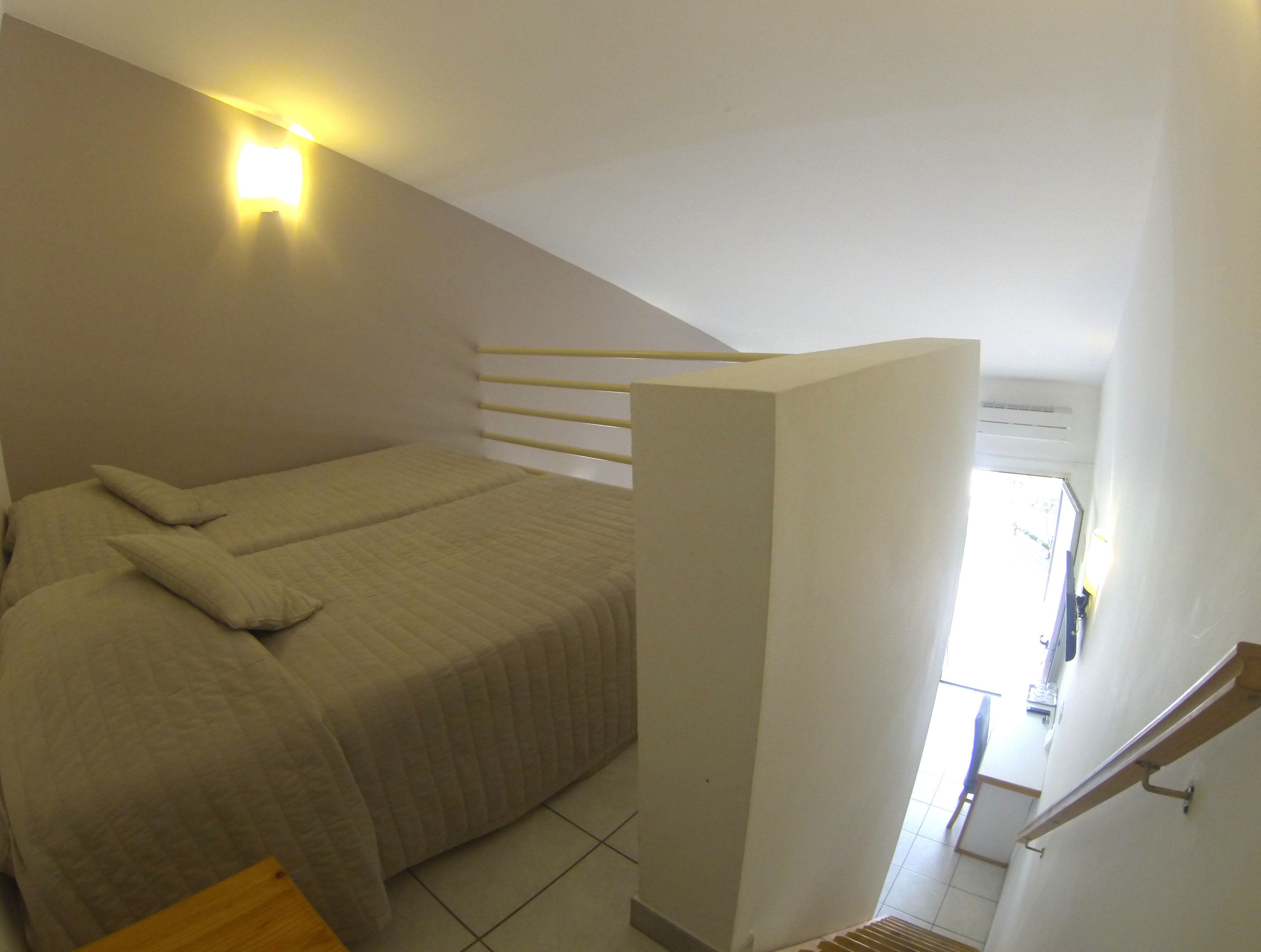 A bedroom with a bed, a nightstand, a wall-mounted light, and a staircase.