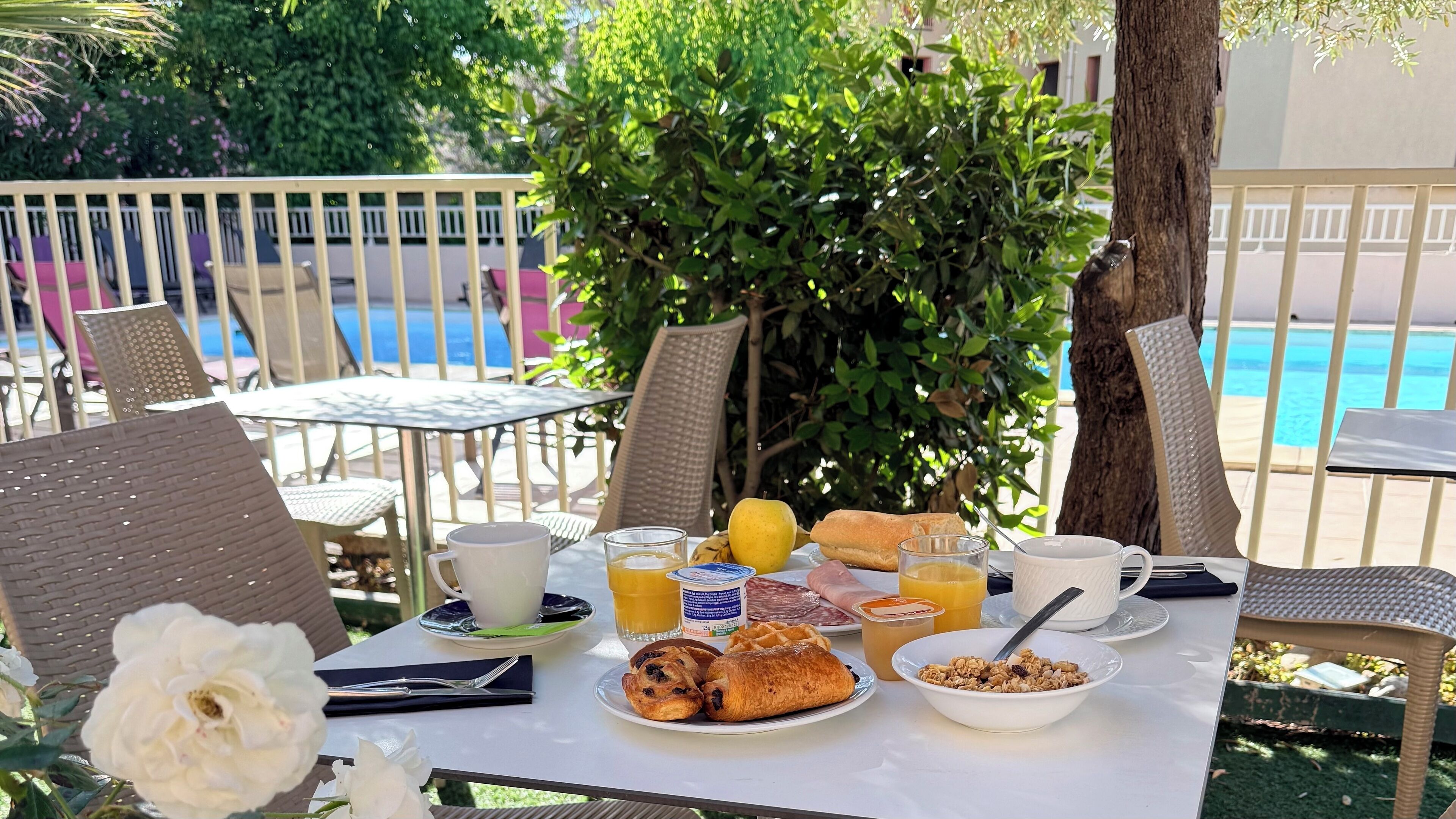 A breakfast table with a variety of food items, a glass of orange juice, and a view of a swimming pool.