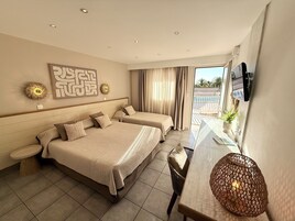 Habitación de hotel con dos camas, una mesa de comedor, un televisor y un balcón con vistas al mar.