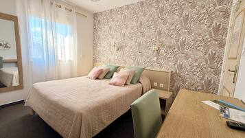 A bedroom with a bed, a desk, a chair, a mirror, and a patterned wall.