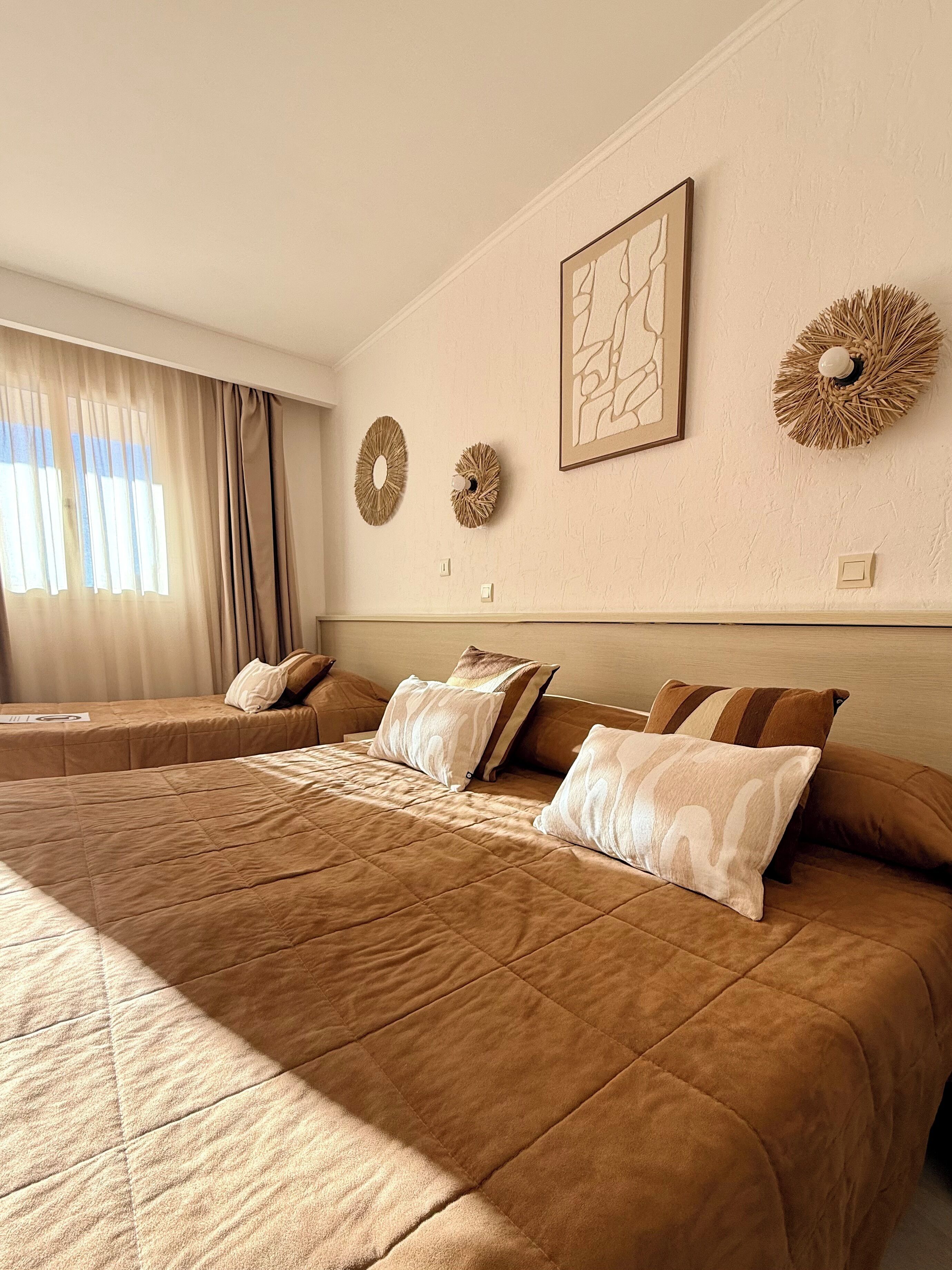 A hotel room with a large bed, two bedside tables, a headboard, and a window with curtains.