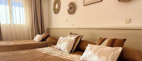 Una habitación de hotel con una cama grande, dos mesitas de noche, un cabecero y una ventana con cortinas.