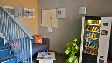 A modern living room with a staircase, a sofa with a cushion, a small coffee table, a plant, and a vending machine.