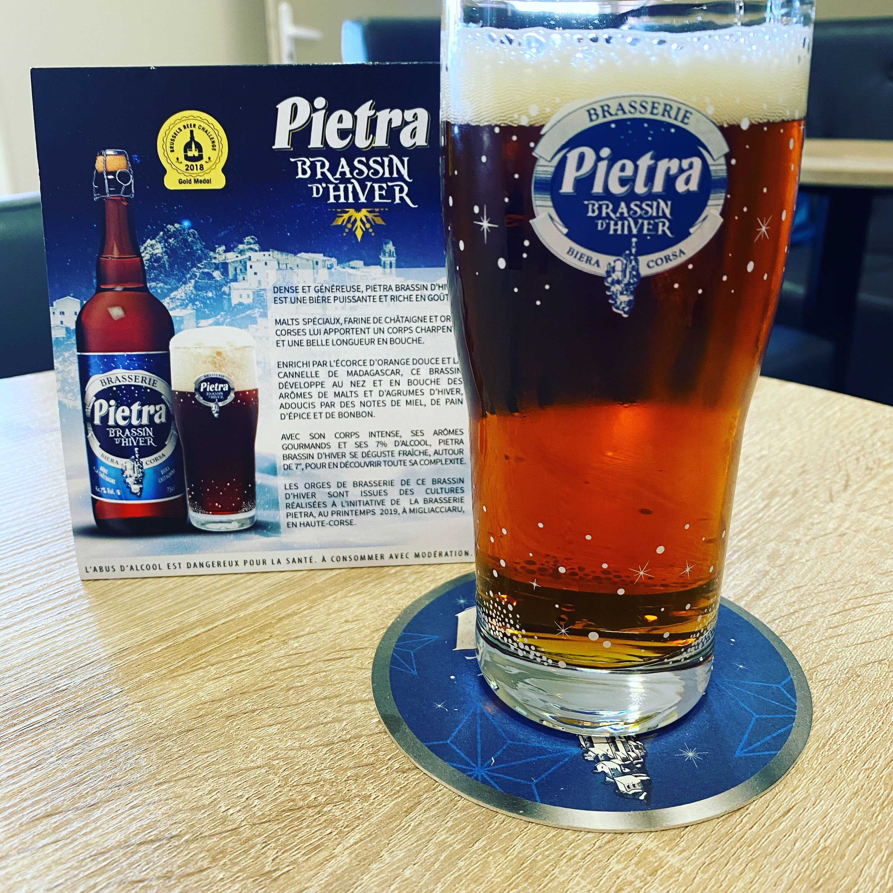 A glass of Pietra Brassin d'Hiver beer with a coaster, and a bottle and glass set beside it.