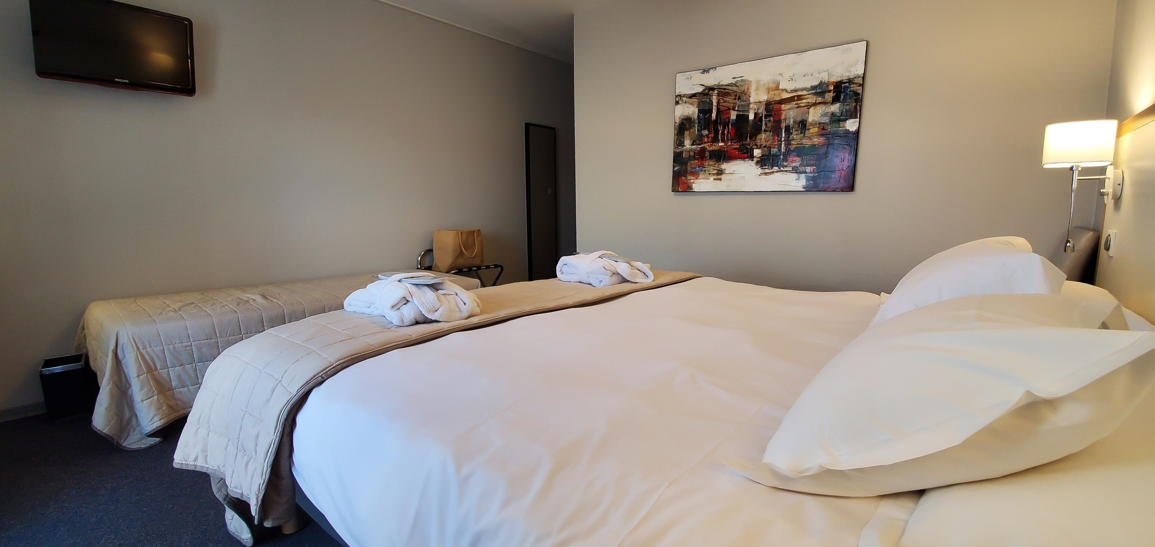 A hotel room with two beds, a flat-screen TV, a painting on the wall, and a bedside lamp.