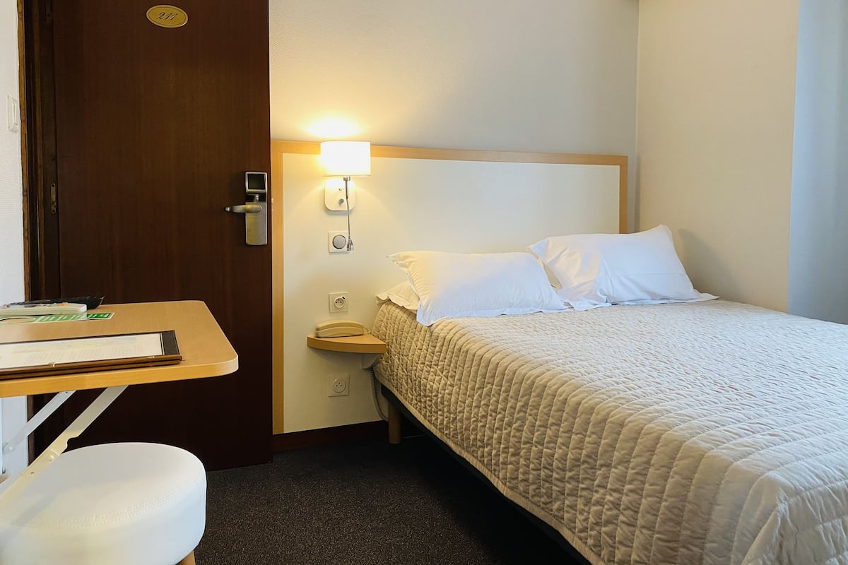 Habitación de hotel con cama, mesita de noche, lámpara, teléfono y puerta con placa numérica.