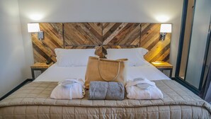 Une chambre d’hôtel avec une tête de lit en bois, deux tables de chevet avec des lampes, un lit recouvert d’une courtepointe beige et des serviettes disposées sur le lit.