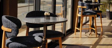 A café with round tables and chairs, large windows, and a wooden floor.