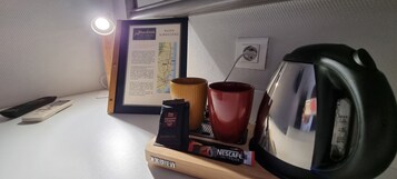 Un escritorio con un directorio enmarcado, una taza roja, un paquete de Nescafé, un control remoto y una tetera.